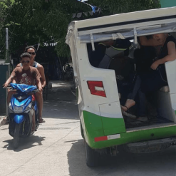 Electric tuk-tuk driving past people on a moped